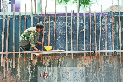 　　烈日下，狹窄的架子上，工人正用錘子固定樁基。