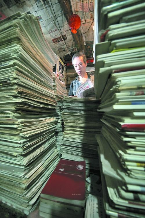 王曉民坐在寫字桌前，被報紙淹沒。