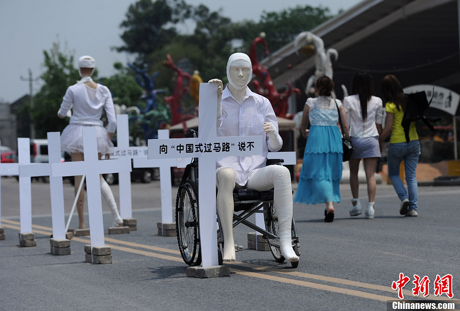 4月16日，重慶市洋人街上擺放著兩個受了傷的塑料人像“模特”，旁邊十字架上寫著向“中國式過馬路”說不