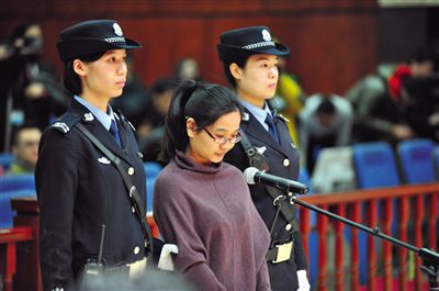 被告人盧梅低著頭，站在朝陽法院刑事審判庭的被告席上。